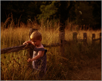 Child Portrait of Little boy in overalls at sunset by fence